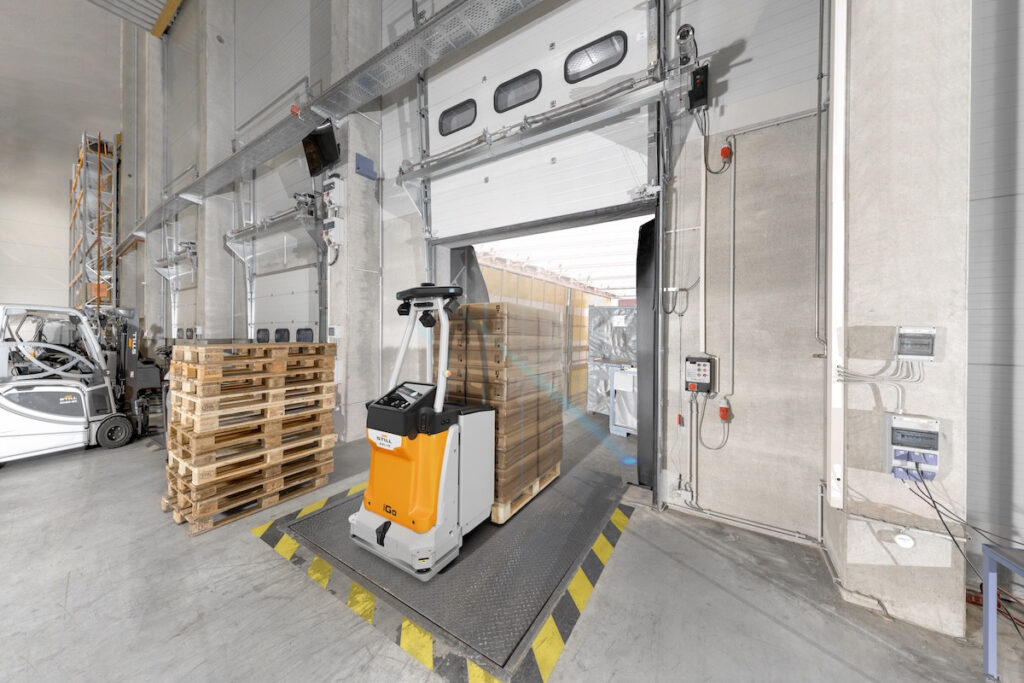 Autonomní vozík STILL AXL 15 iGo vjíždí s paletou do kamionu u nákladové rampy.
