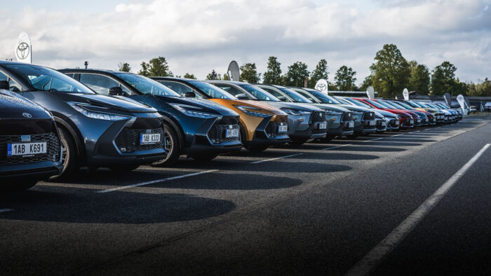 Dlouhá řada moderních automobilů Toyota různých barev, včetně nového C-HR, zaparkovaná v přesné diagonální linii na venkovním polygonu během předváděcí akce pro firemní flotily.